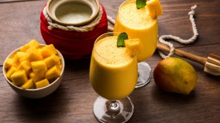 A close-up shot of mango lassi or smoothie in big glasses with curd, cut fruit pieces and blender