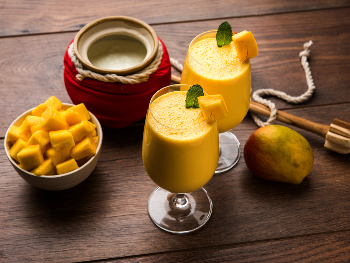 A close-up shot of mango lassi or smoothie in big glasses with curd, cut fruit pieces and blender