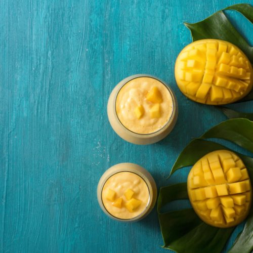 A flat lay picture of mango lassi drink in glasses and mangoes on tropical leaves