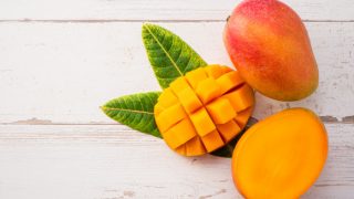 Fresh ripe mango - whole and sliced on a light wooden background