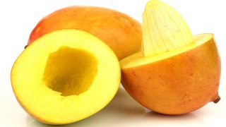 Close up of whole and sliced mangos with a seed visible on a white background
