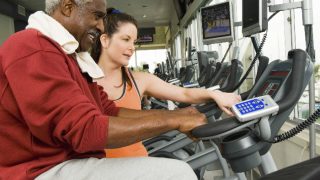 Gym instructor helping older man on treadmill