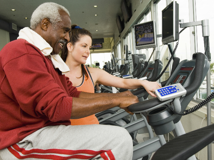 Gym instructor helping older man on treadmill