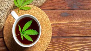 A cup of marijuana tea with fresh marijuana leaf placed on top