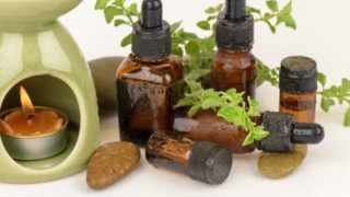 Containers of marjoram essential oil and fresh leaves on a white background