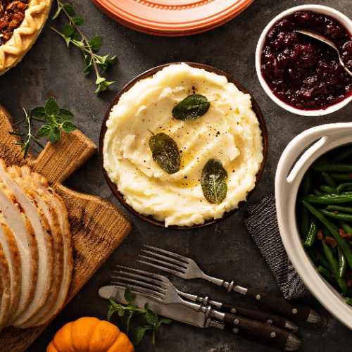 A flatlay picture of mashed potatoes with butter and sage, side dish for Thanksgiving or Christmas dinner, kept next to asparagus, baked beans and turkey slices.