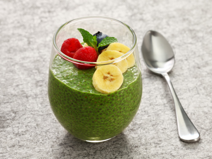 Matcha chia pudding in a glass topped with berries, mint leaves and banana