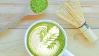 Flatline picture of a spoon of matcha powder, a cup of matcha tea and wooden whisk.