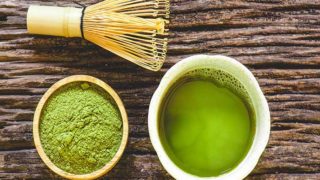 Flatline picture of green liquid in a cup, green powder in a bowl and whisk on a wooden surface.