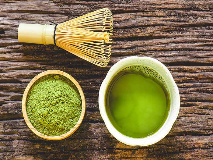 Flatline picture of green liquid in a cup, green powder in a bowl and whisk on a wooden surface.