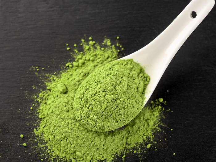 Matcha powder in white ceramic spoon and tea leaves on black background