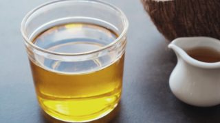 A glass and a small kettle of MCT oil (medium-chain triglycerides oil )with fresh halved coconut on a grey table