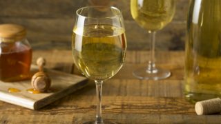 Mead, or honey wine, in wine glasses with a honey jar and wine bottle in the background