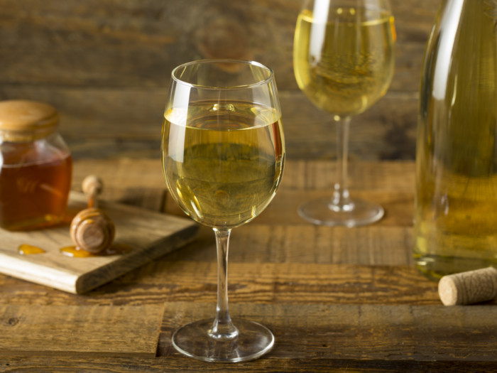 Mead, or honey wine, in wine glasses with a honey jar and wine bottle in the background