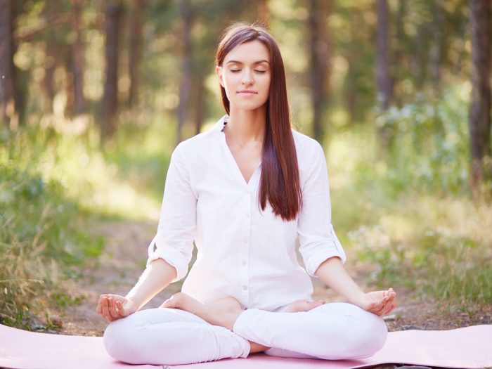 A woman meditating on a pink yoga mat in the outdoors