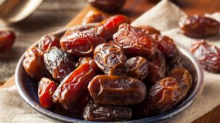A wooden bowl of dried medjool dates on a wooden table