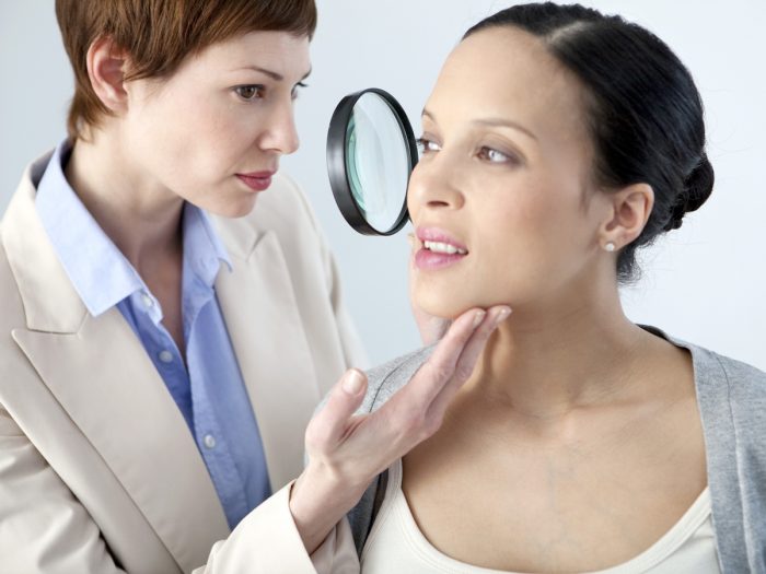 A woman doctor checking a patient's face through a magnifying glass