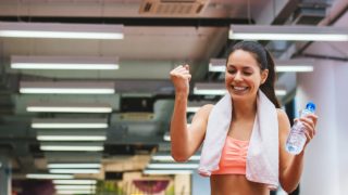 A woman in gym clothes with a mineral water bottle, looking happy and excited
