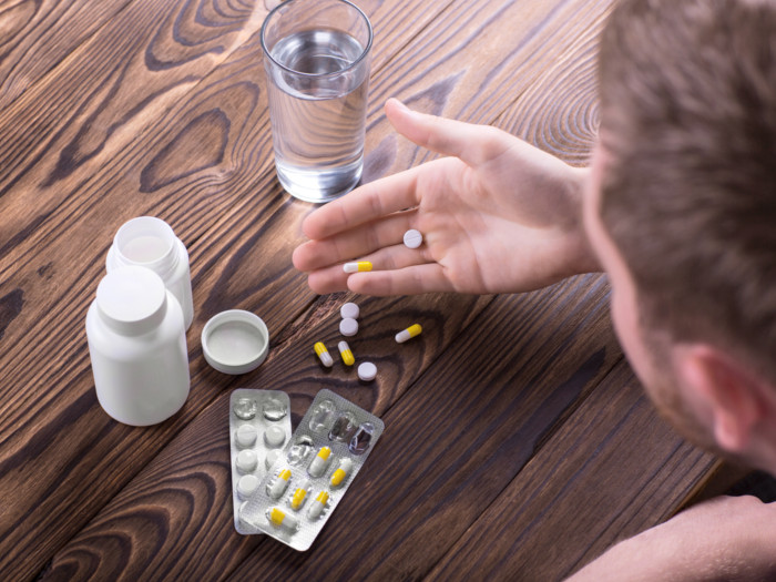 Pills and bottles with a glass of water placed on a table while a man looks at them in his hand