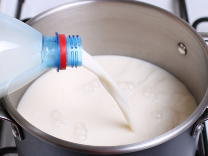 Pouring fresh milk out of a plastic bottle into a saucepan