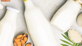 Bottles of milk lying on a white surface with spoons full of almonds, rice, and coconut