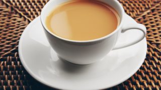 Cup and saucer of tea on a woven cane surface.