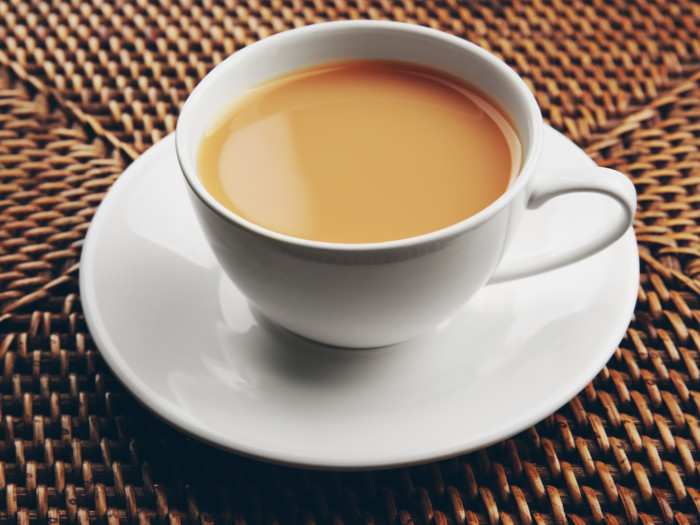 Cup and saucer of tea on a woven cane surface.