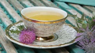 A cup of milk thistle tea with milk thistle blossoms on a blue wooden table