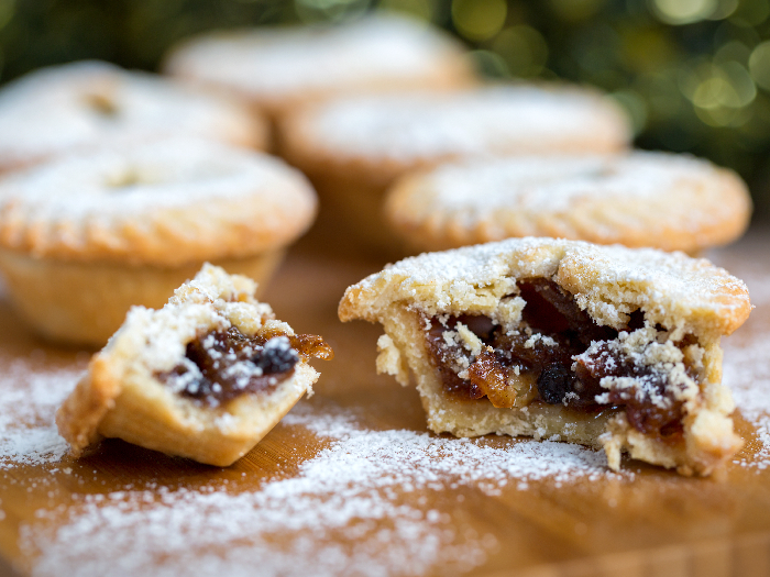 Closeup of an open mince pie on a wooden board with green christmas background