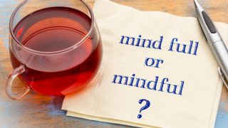 A cup of red-colored tea, kept on a napkin with the message "Mind full or mindful?"