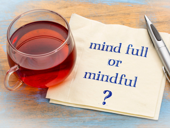 A cup of red-colored tea, kept on a napkin with the message "Mind full or mindful?"
