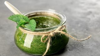 A close up shot of a jar containing mint sauce placed atop a grey platform