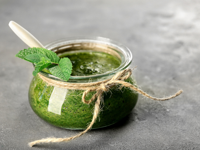 A close up shot of a jar containing mint sauce placed atop a grey platform