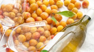Two wine glasses and a glass bottle placed over a bed of plums.