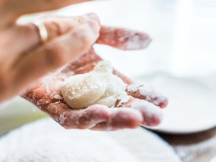 Hands shaping a piece of mochi sticky glutinous rice cake dusted with starch flour to make dessert