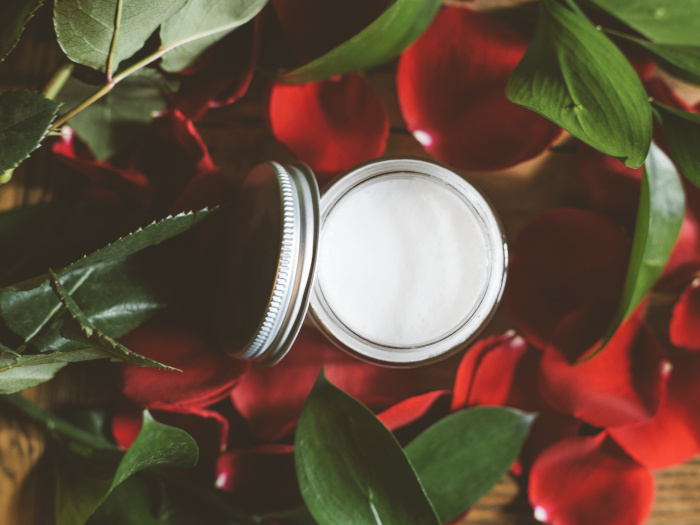 White cream in a jar in between red and green petals and leaves