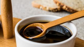 A white bowl filled with molasses with a wooden spoon on a wooden table