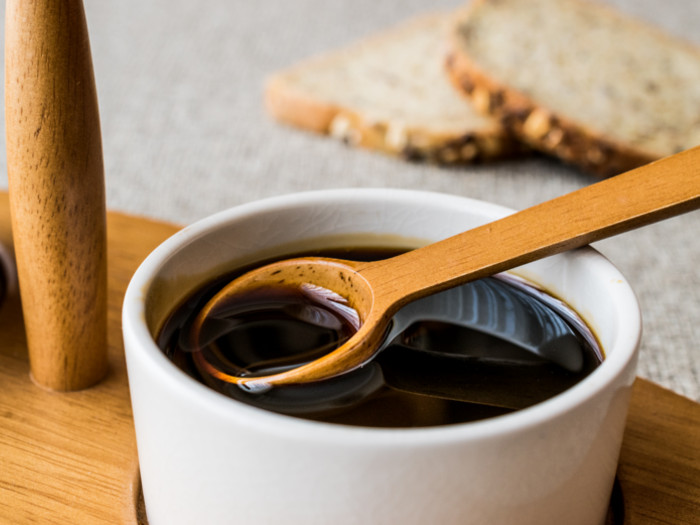 A white bowl filled with molasses with a wooden spoon on a wooden table