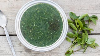 Green molokhia soup in a white bowl with fresh green leaves on a wooden table