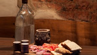 A glass bottle of moonshine kept next to bread slices and meat atop a wooden platform