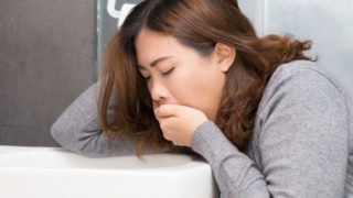 A woman about to throw up over a toilet bowl