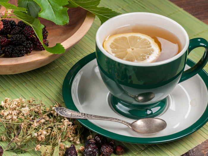 A cup of tea with a lemon slice next to mulberries