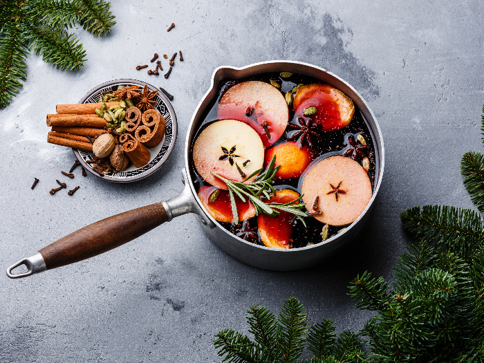 Mulled wine hot drink with citrus, apple, and spices in an aluminum casserole and Fir branch on concrete background