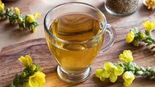 Mullein Tea in a glass cup kept atop a wooden platform, next to mullein flowers
