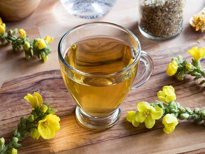 Mullein Tea in a glass cup kept atop a wooden platform, next to mullein flowers