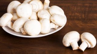 A white plate filled with white mushrooms on a wooden table