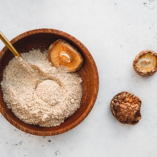 A flat lay picture of dried shitake mushroom and its powder kept atop a white platform