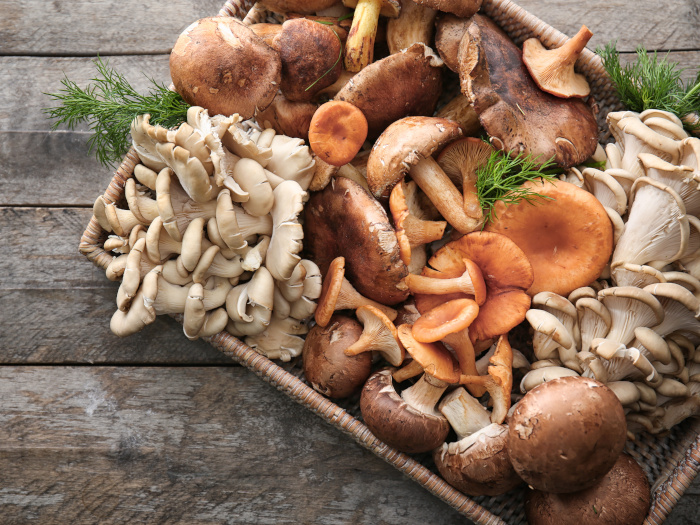 A wicker tray with a variety of raw mushrooms on a wooden table