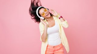A happy girl with goggles on, listening to music on headphones and dancing