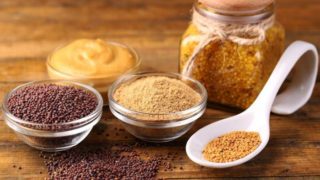 Whole mustard seeds, mustard powder, and bottled mustard on wood